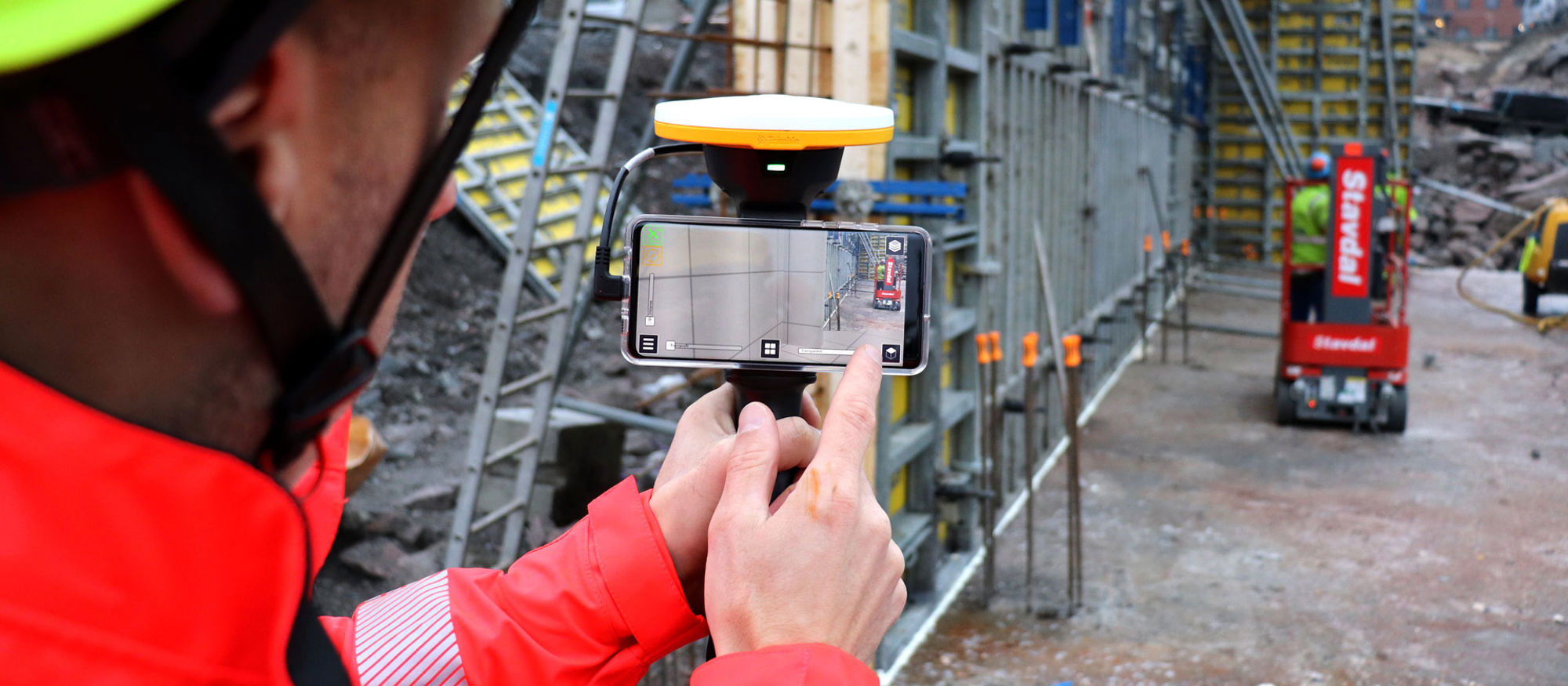 Person står och mäter genom en mobiltelefon på en byggarbetsplats.