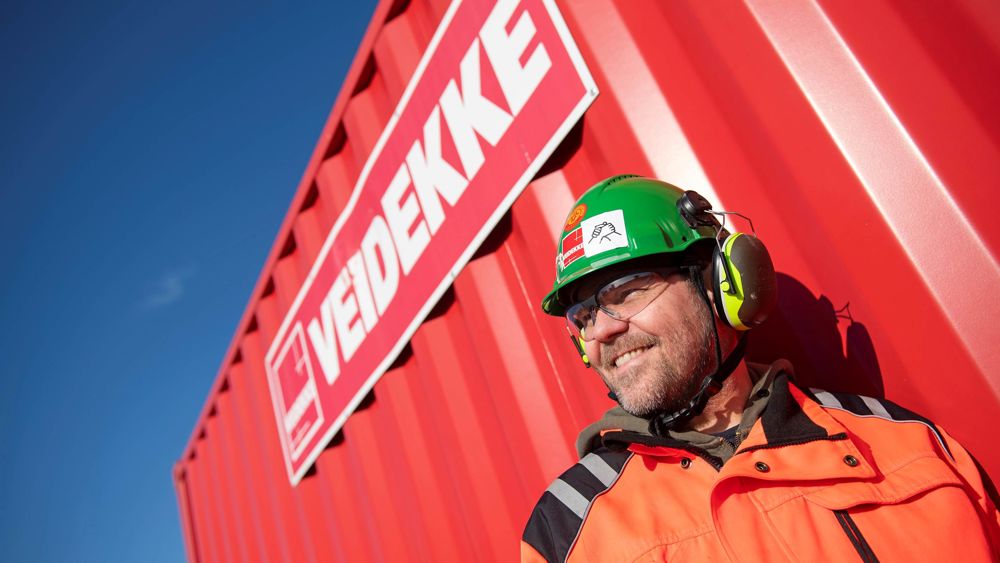 Foto av en person i varselkläder framför en byggcontainer