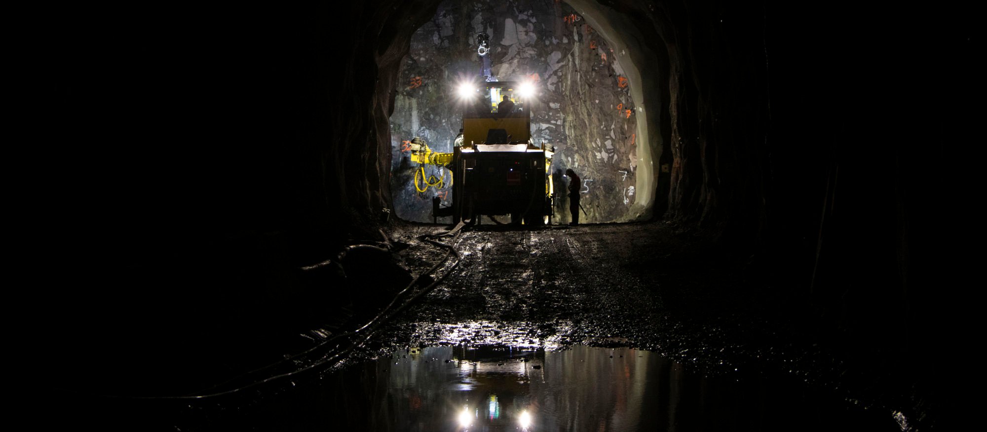 Mörk bild av underjordisk tunnel där en maskin arbetar med strålkastarna på längst in