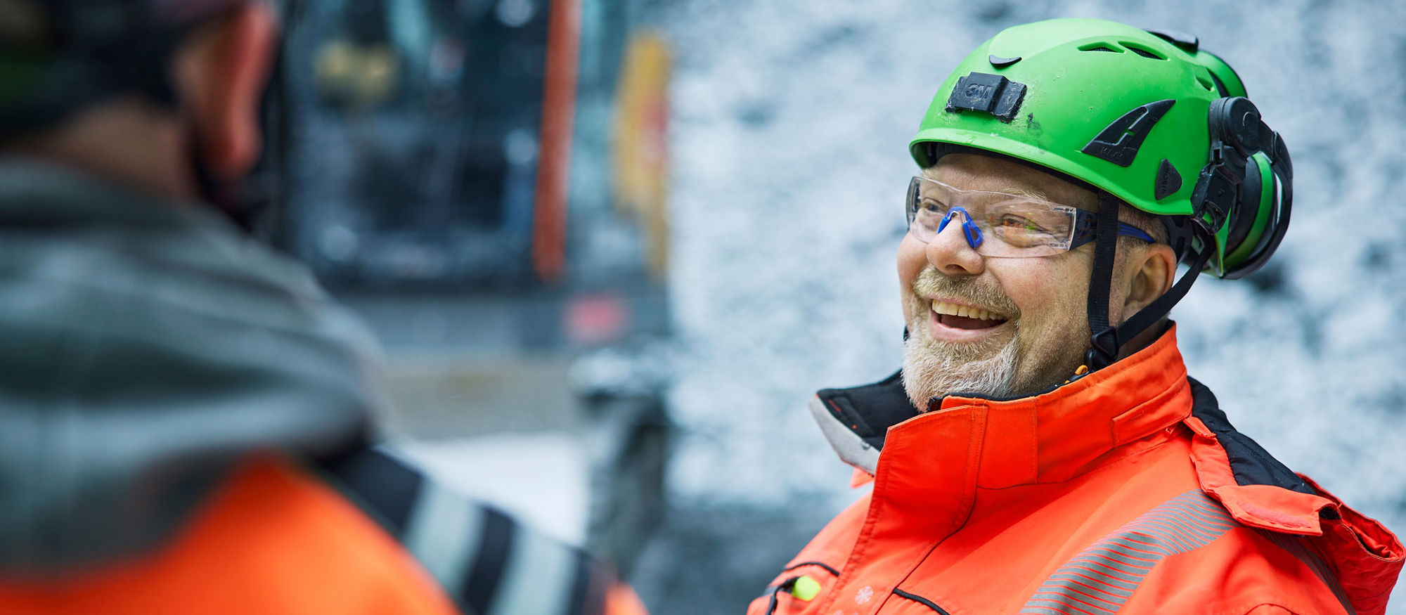 Leende anläggningsarbetare iklädd varseljacka och hjälm.