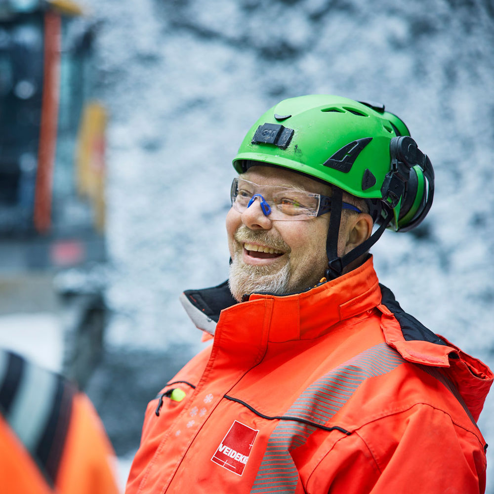 Leende anläggningsarbetare iklädd varseljacka och hjälm.