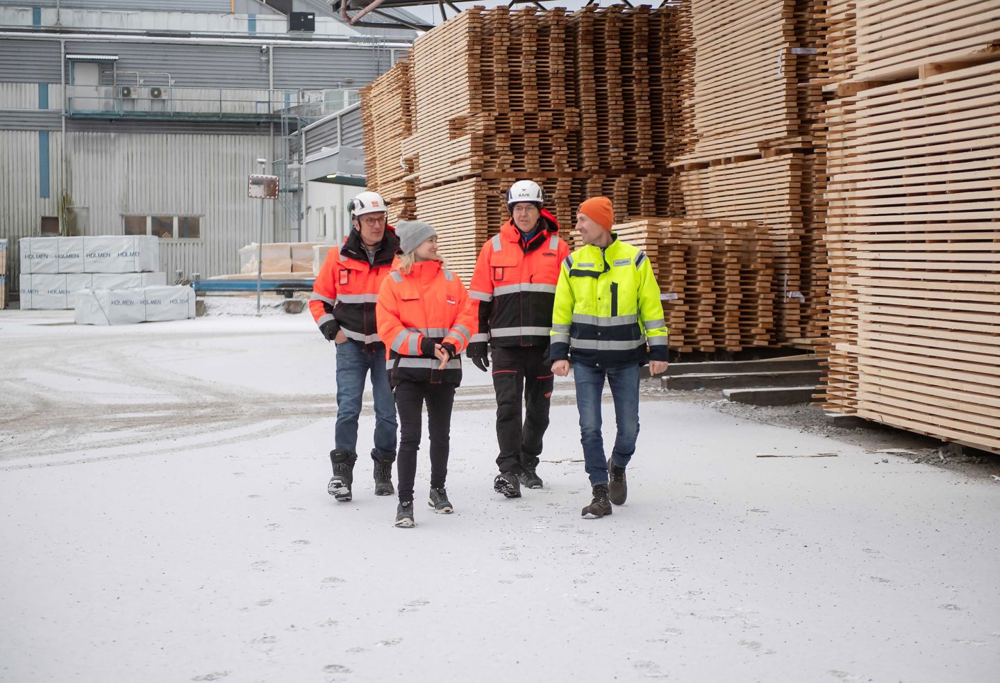 Gruppbild. Fyra personer i varselkläder går mellan brädstaplarna utanför hyvleriet. 