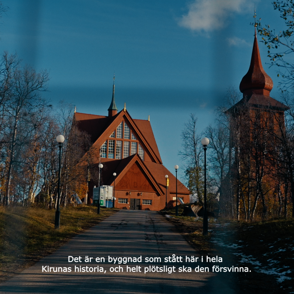 Thumbnail-bild från film om flytten av Kiruna kyrka. Här syns den röda kyrkan med sin klockstapel på en kulle i slutet av en gångväg. 